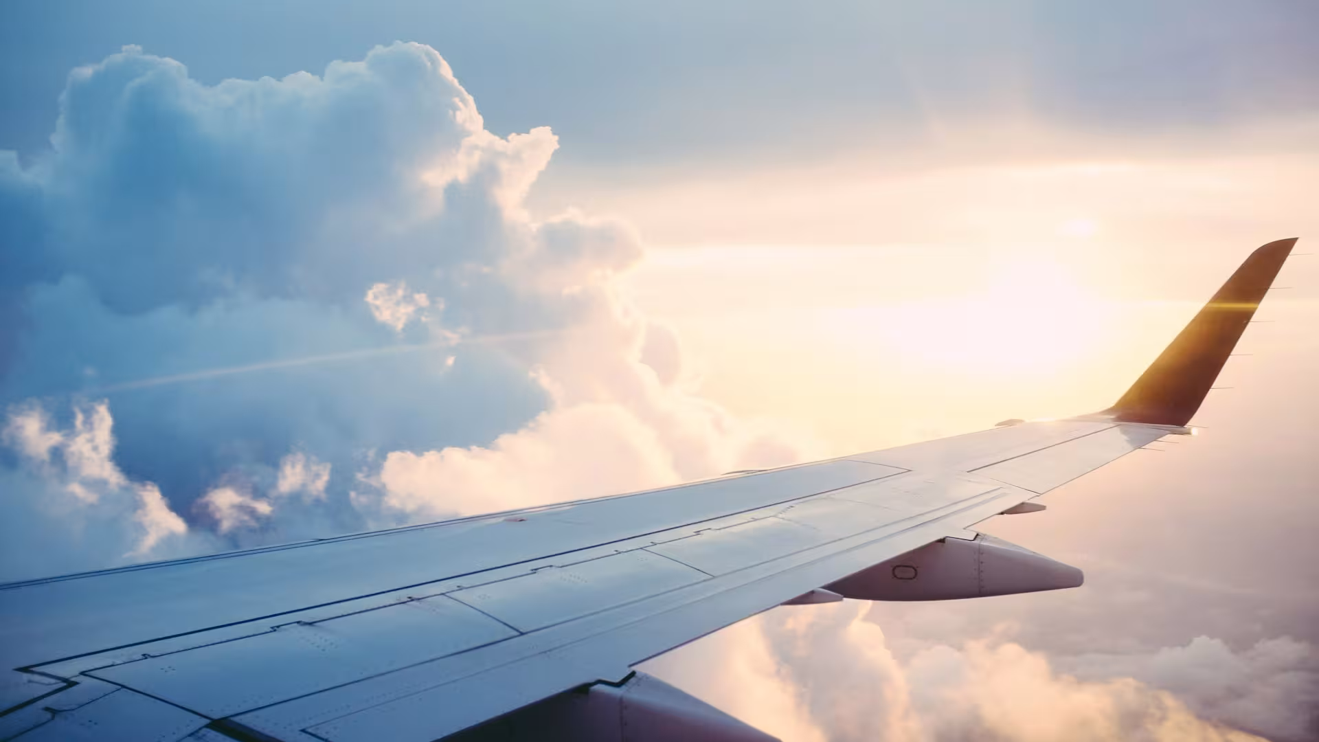 Asa de avião voando sobre as nuvens no horizonte ao entardecer